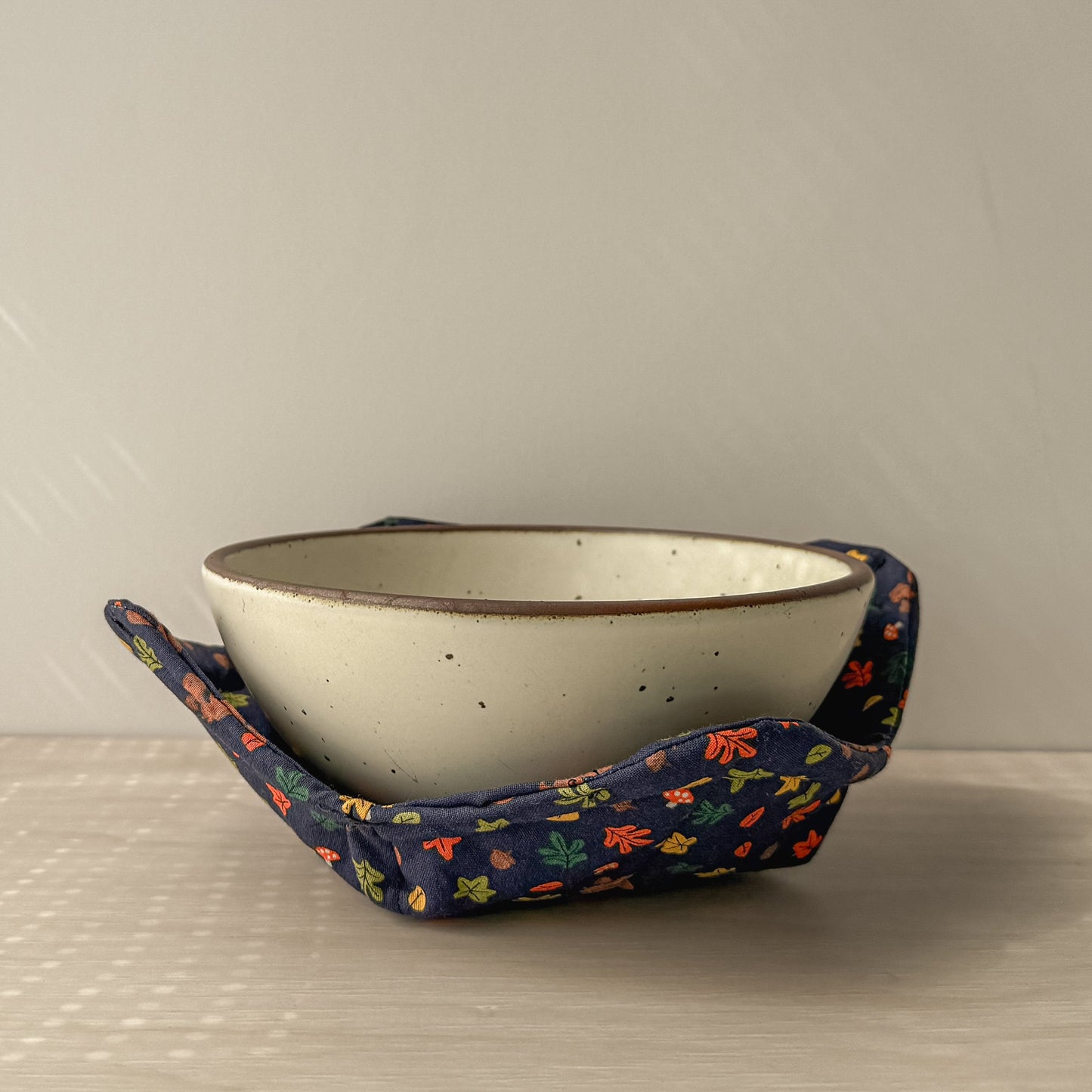 Ceramic bowl in a bowl cozy made with with fall decor fabric of leaves acorns squirrels on a blue backgroundc