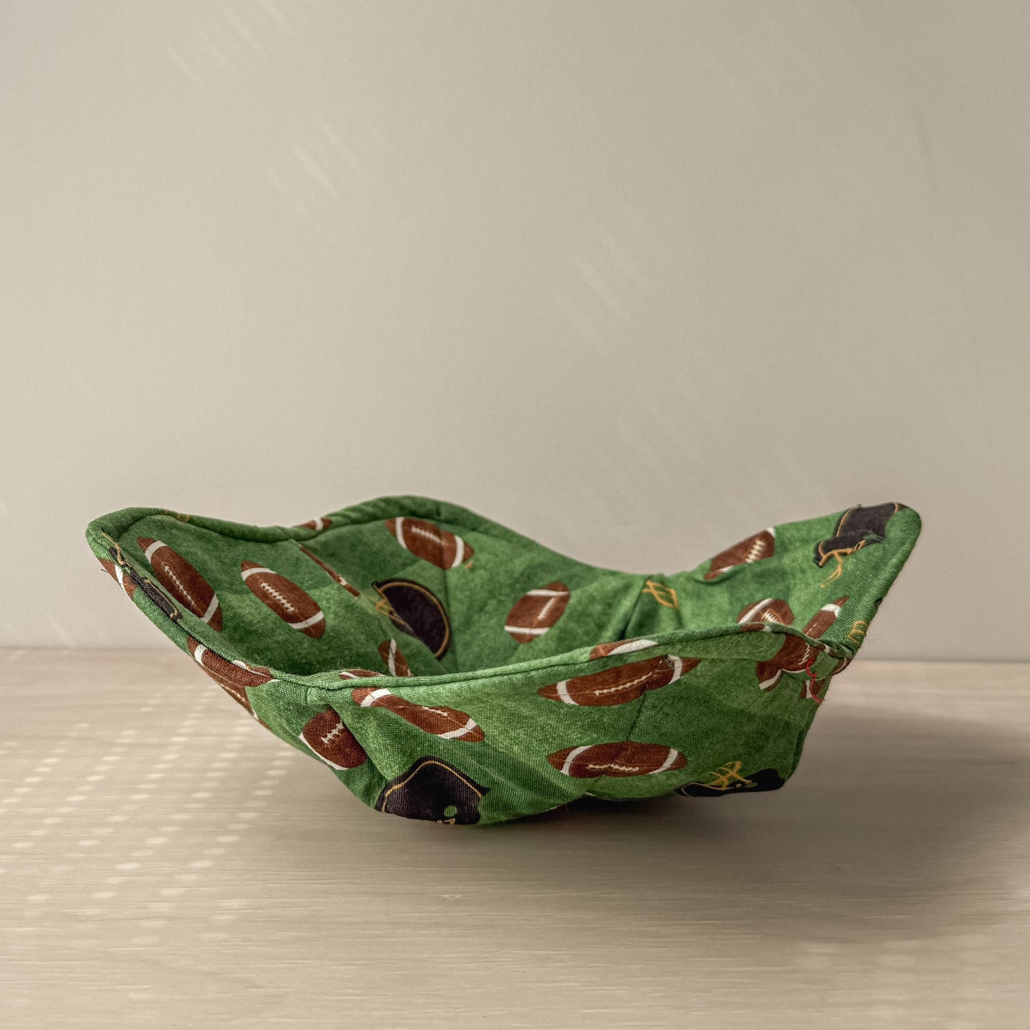 Green bowl cozy with football themed material on a neutral background