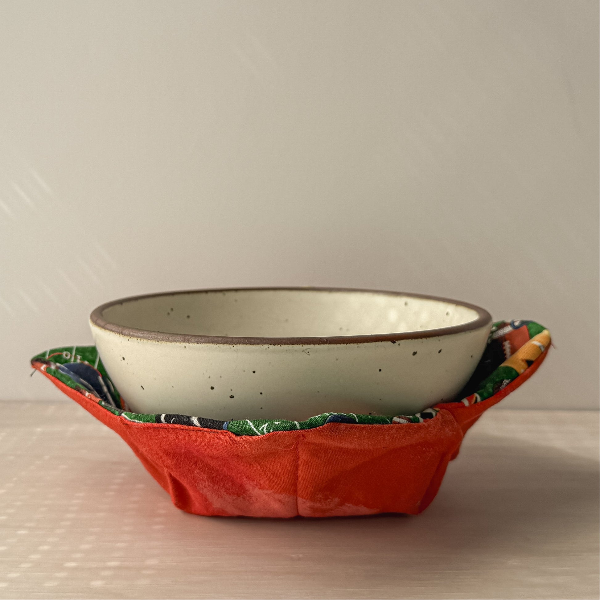 Ceramic bowl in a bowl cozy of fooball helmets and an orange fabric against a plain background